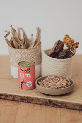 Bowell’s Pute-Komplettmenü für Hunde neben Kauartikeln und Hundenapf